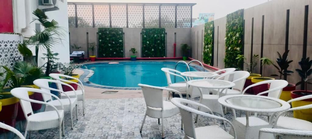 An indoor swimming pool with white chairs and tables around it, surrounded by potted plants and a modern architectural design.