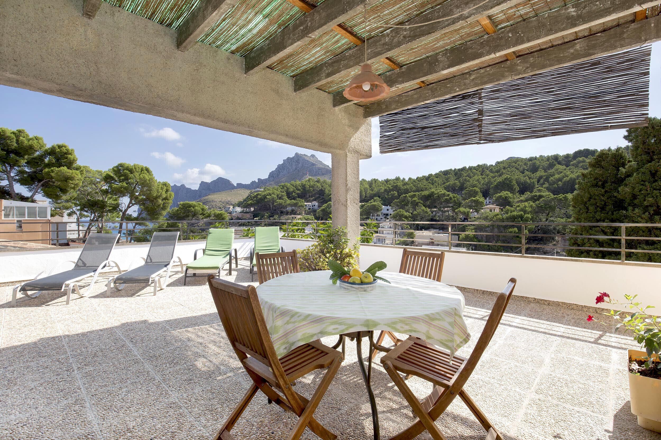 An outdoor patio with a table and chairs, a fruit bowl, and a view of a mountainous landscape.
