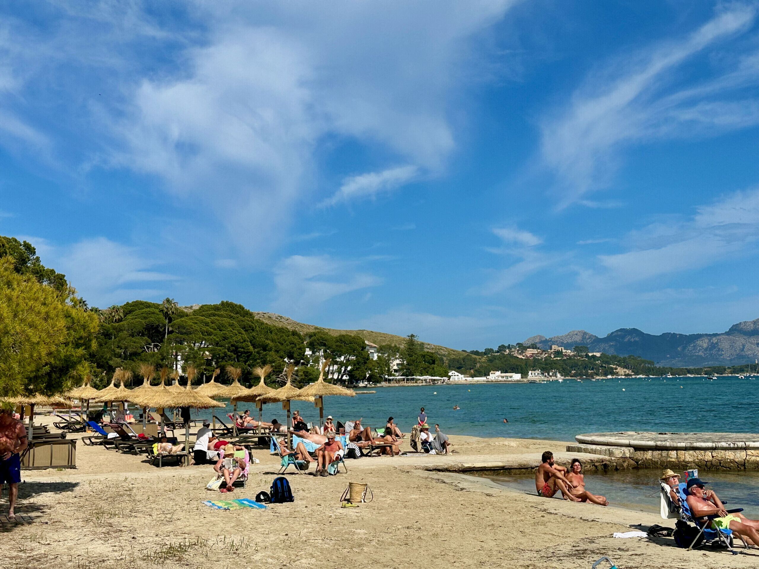 Una playa con gente tomando el sol y nadando, rodeada de árboles y colinas.