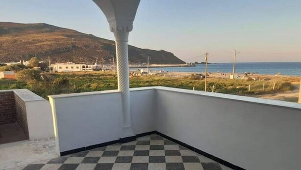 Ein Balkon mit kariertem Boden, weißen Wänden und Blick auf Strand und Berge.