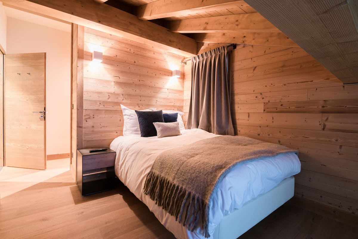 Une chambre aux murs lambrissés, avec un lit, une table de chevet et une porte donnant sur une autre pièce.