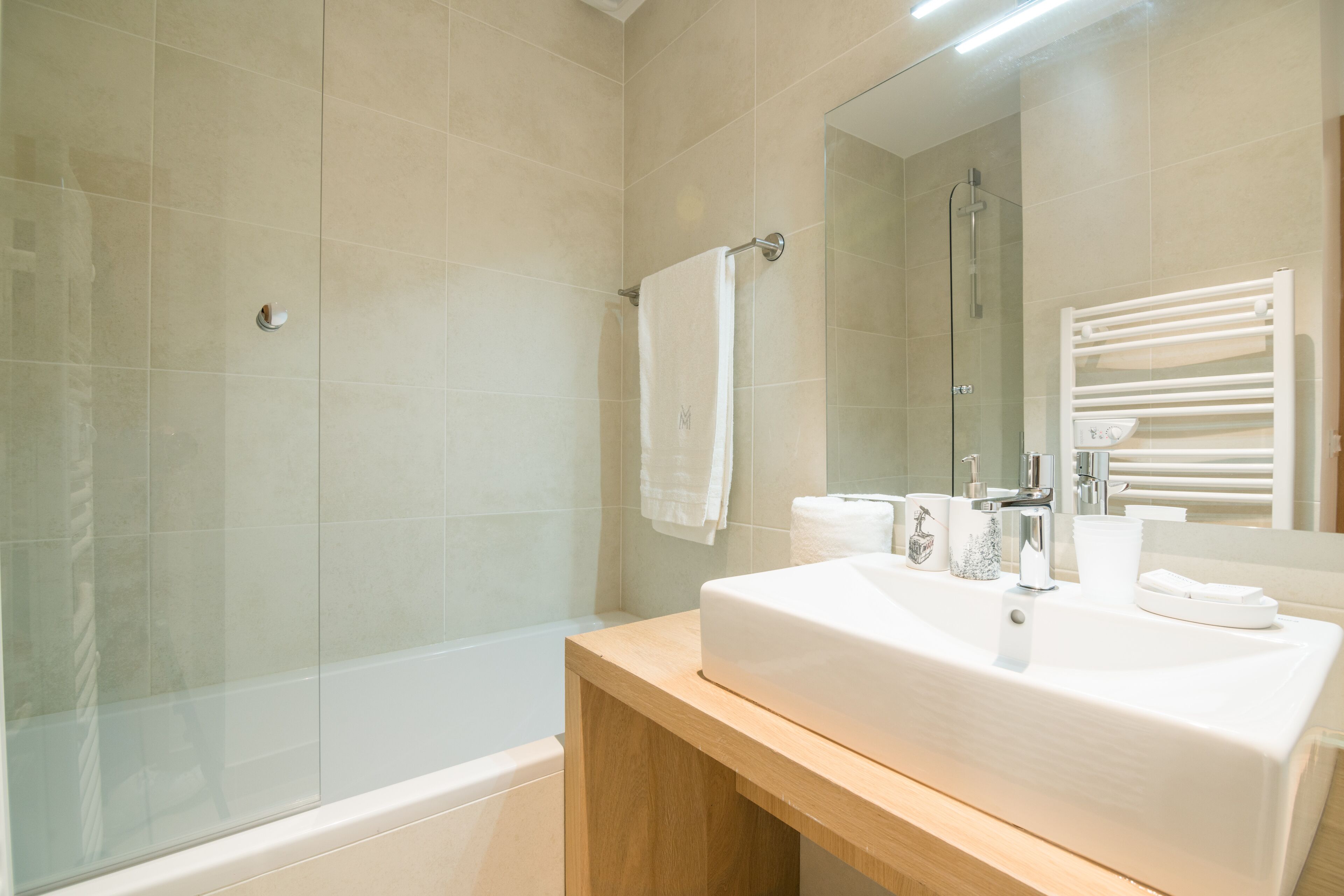 A modern bathroom with a large sink, a glass shower enclosure, and a mirror reflecting a towel rack.