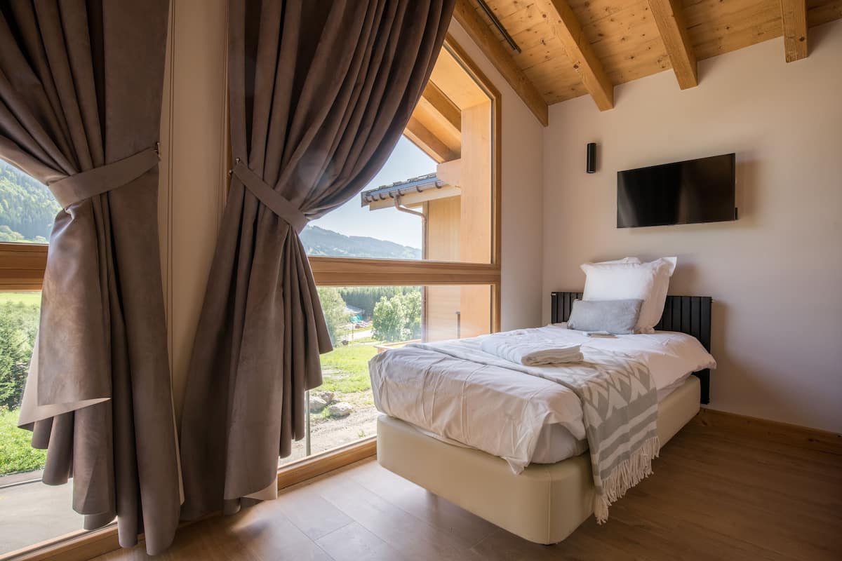 Une chambre à coucher avec un lit, des rideaux, un téléviseur et une vue sur l’extérieur.