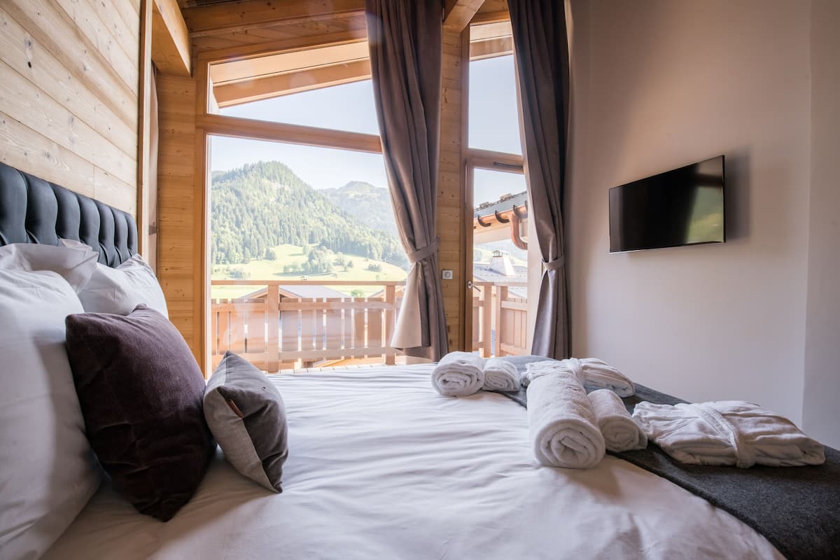 Une chambre à coucher avec un lit, des oreillers, des serviettes, une télévision et une vue sur une montagne boisée.