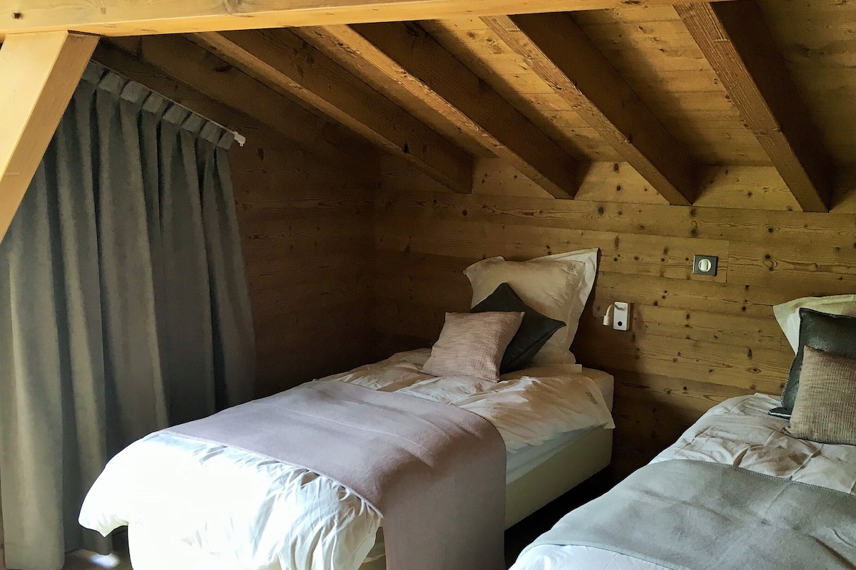 Une chambre confortable avec deux lits, des poutres apparentes en bois au plafond et un rideau.