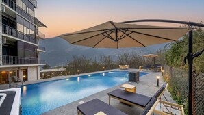 A swimming pool with lounge chairs and umbrellas, surrounded by a building with balconies and a mountainous backdrop. - Echor Himalayan Aurum Resort & Spa, Manali (Manali)