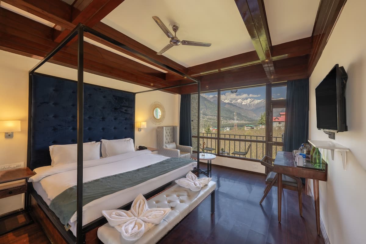 Una cama con dosel con vistas a las montañas, un ventilador de techo, un escritorio con una silla y una mesita con una botella y vasos.