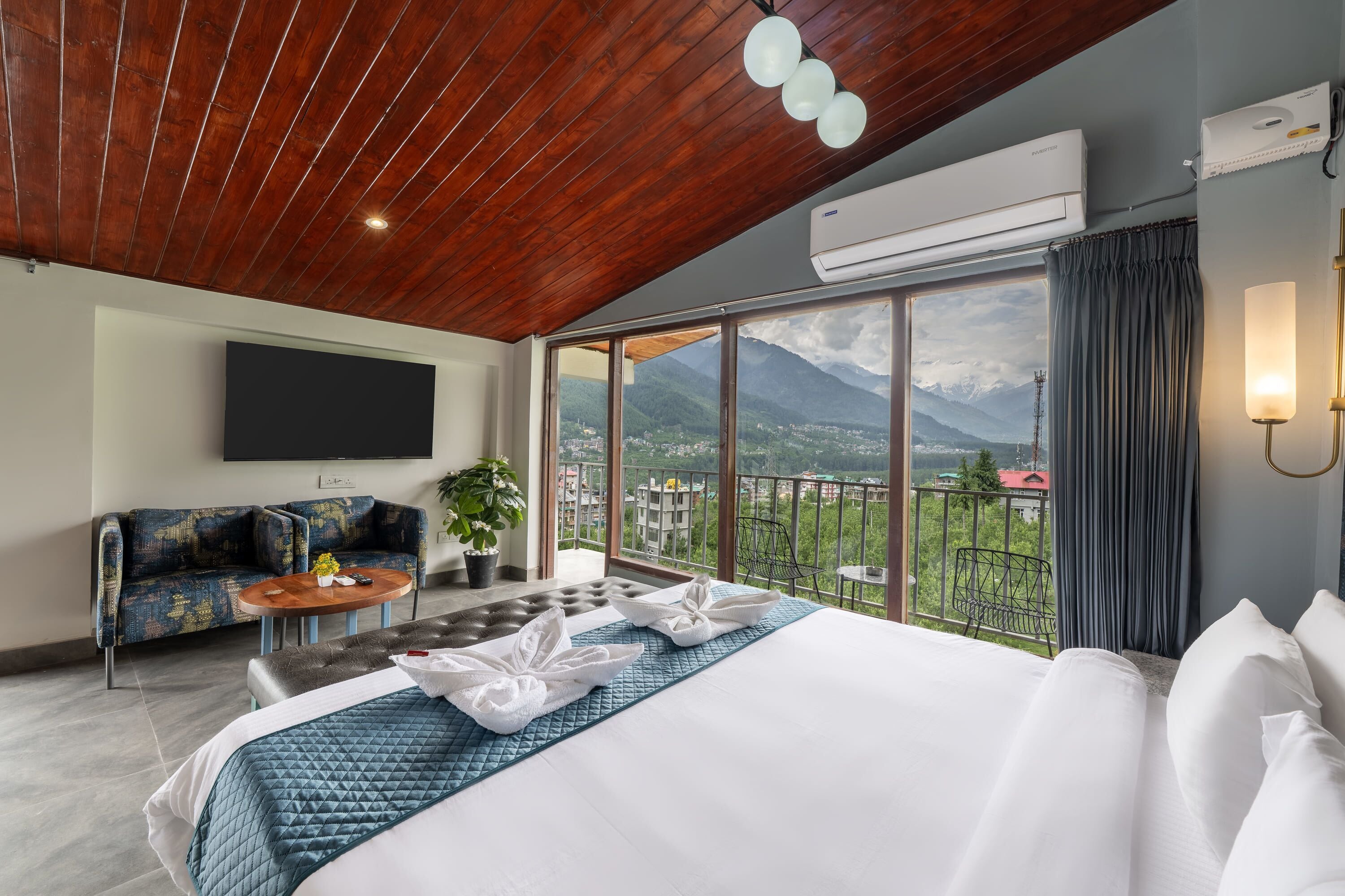 Una habitación de hotel moderna con una cama grande, un sofá, una mesita y un balcón con vistas a la montaña.