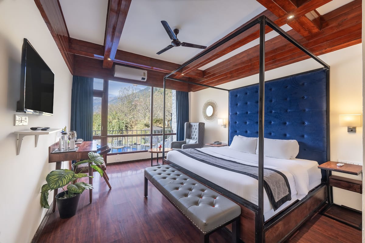 Una cama con dosel y cabecera tapizada, ventilador de techo, televisor de pantalla plana y balcón con vistas al exterior.