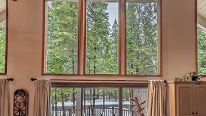 A spacious room with large windows, a wooden deck, and a view of trees. - Evergreen Pinecone Cottage • Hot Tub • Pool Access • Espresso • A/C (Dorrington)