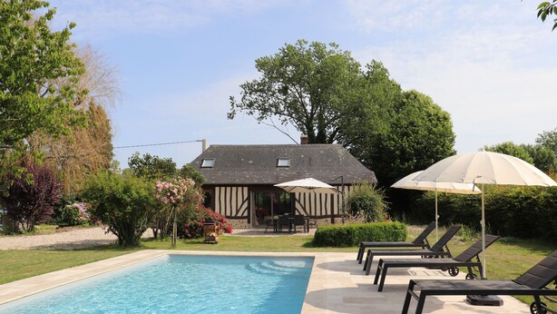 Une piscine avec des chaises longues et des parasols, une maison en arrière-plan et une végétation luxuriante tout autour.