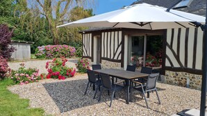 Une terrasse avec une table et des chaises, un parasol blanc et un mur en pierre.