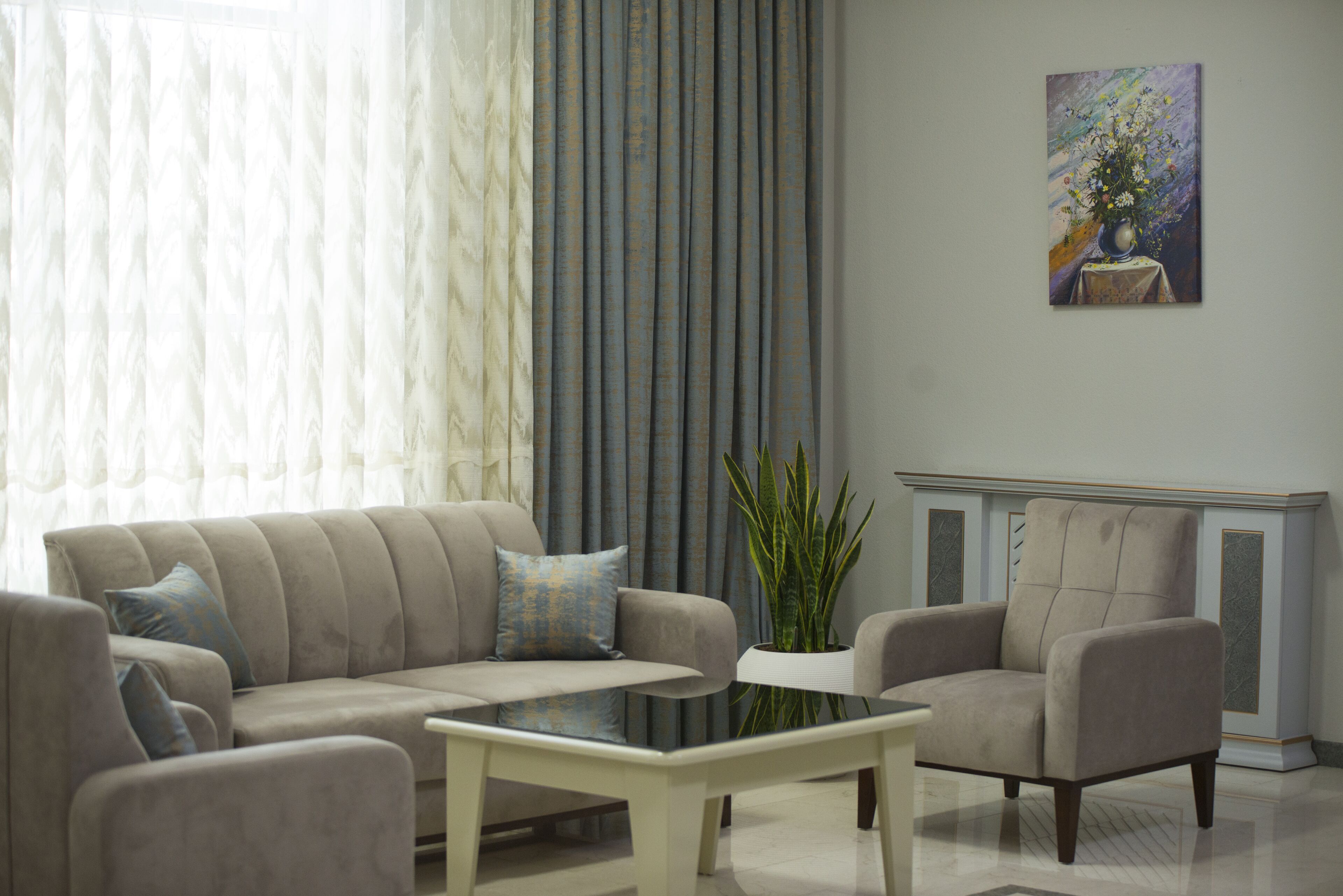 A living room with a sofa, armchairs, a coffee table, and a potted plant.