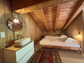 A wooden cabin bedroom with a single bed, a round mirror, a white sink, and a patterned rug.