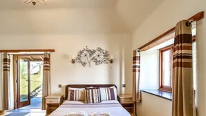 Un dormitorio con una cama grande, suelo de madera, un candelabro, una ventana con cortinas y vistas al exterior.