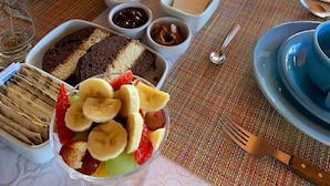 A breakfast setting with bread, pastries, fruit, and beverages on a table. - Chalés Vista Linda (Santo Antonio do Pinhal)