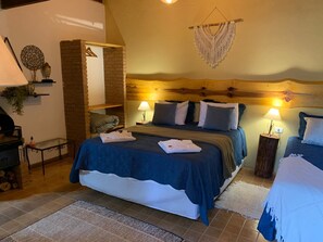 A cozy bedroom with a large bed, two bedside lamps, a hanging macrame decoration, and a brick wall feature. - Chalés Vista Linda (Santo Antonio do Pinhal)
