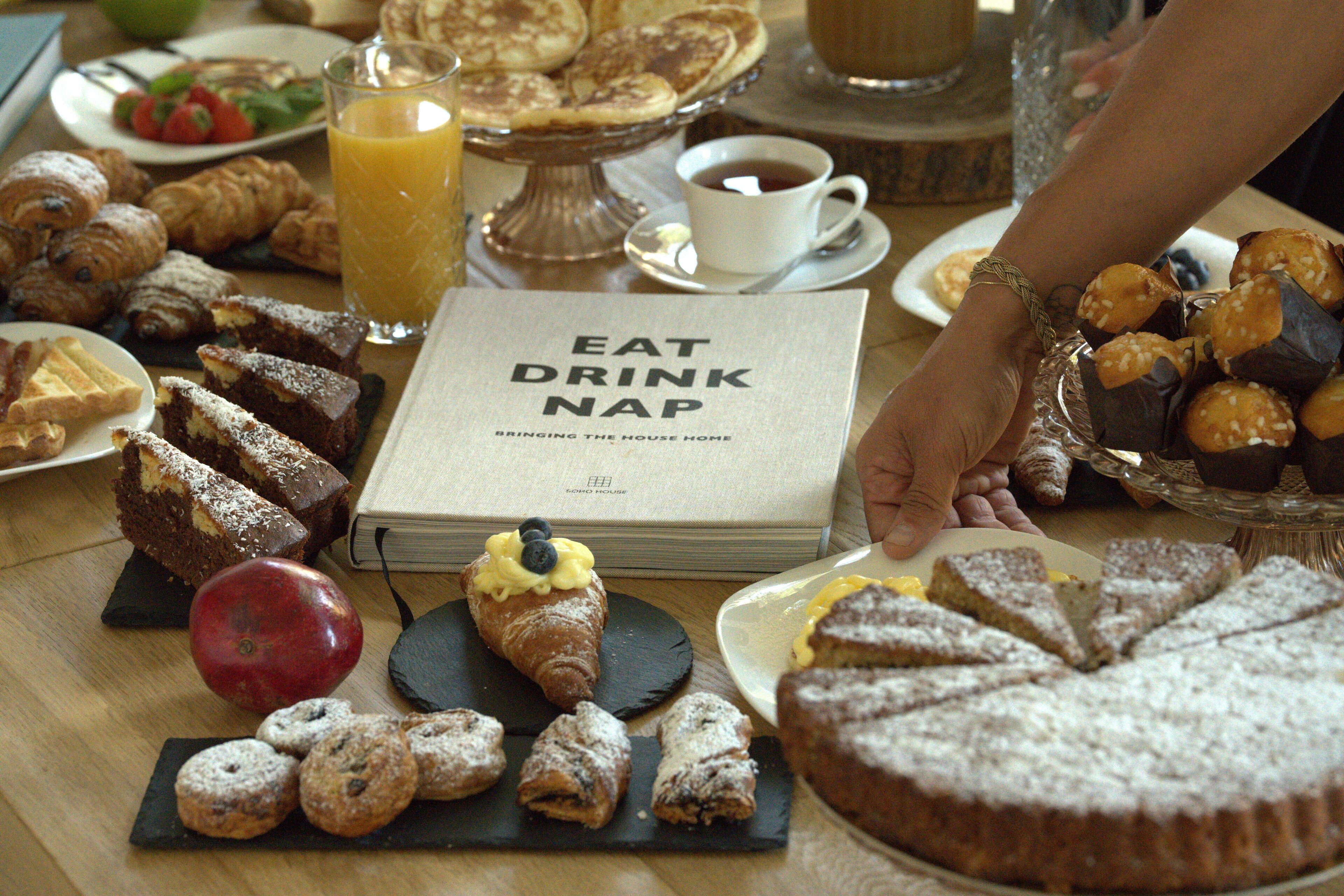 A breakfast spread with pastries, a book titled "EAT DRINK NAP", and a glass of orange juice.
