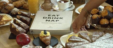 A breakfast spread with pastries, a book titled "EAT DRINK NAP", and a glass of orange juice.