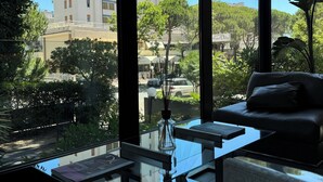 A modern living room with a glass coffee table, a sofa, and a view of a cityscape and greenery. -  M House Art Hotel (Cervia)
