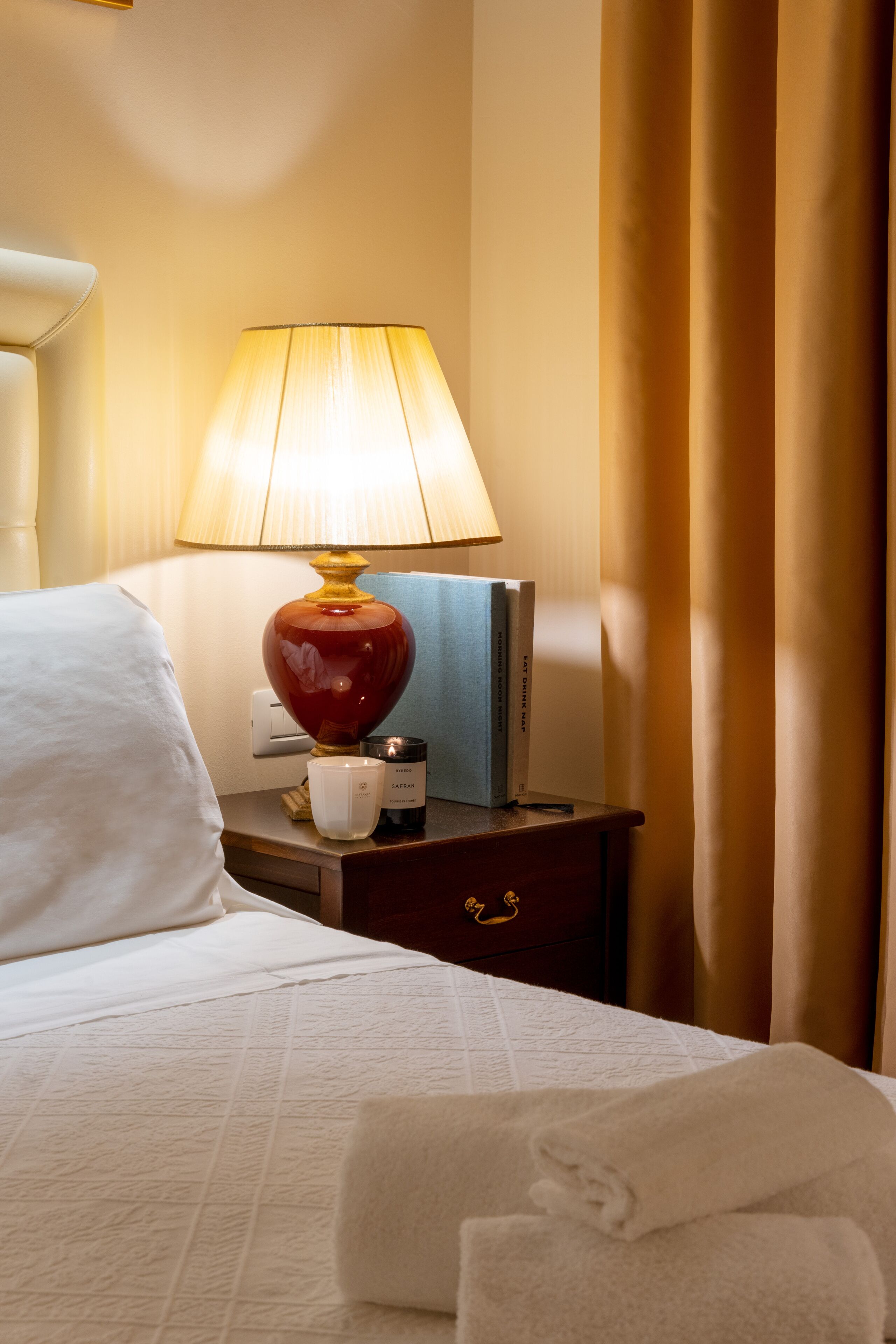 Una camera d'albergo con un letto rifatto, una lampada da comodino, un libro e una candela sul tavolino.