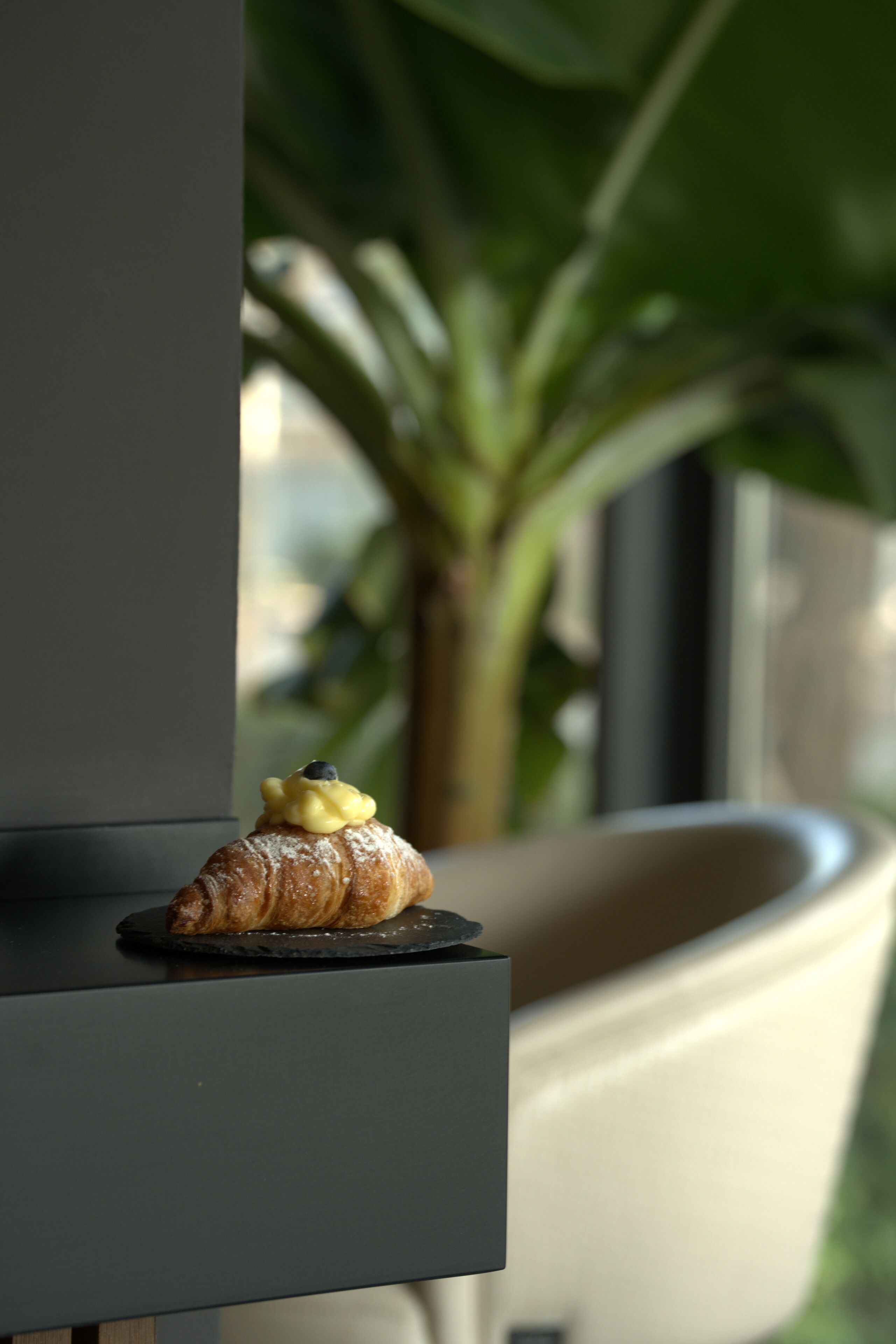 A croissant with a blueberry on a dark plate on a shelf.