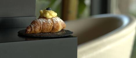 A croissant with a blueberry on a dark plate on a shelf.