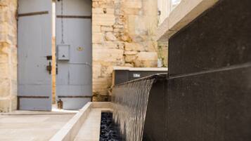 A stone building with a large gray door and a black water feature.