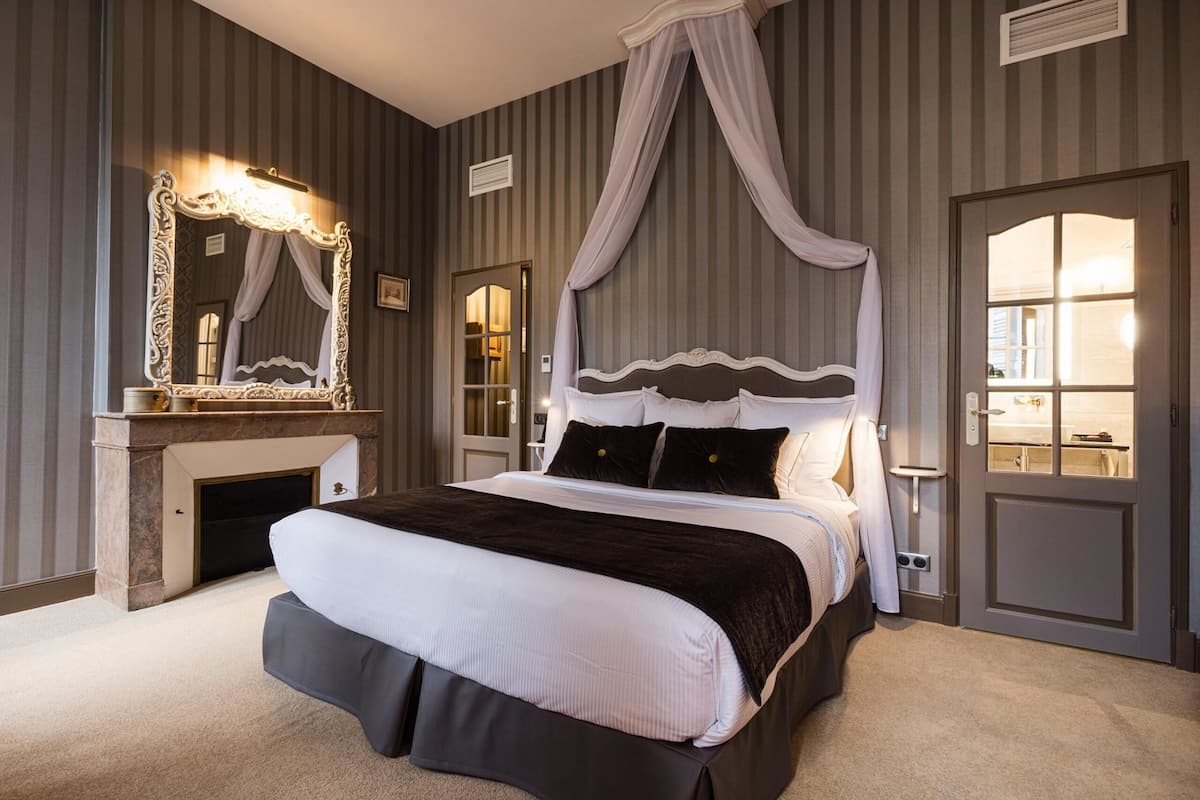 A bedroom with a four-poster canopy bed, a fireplace, and a large mirror.