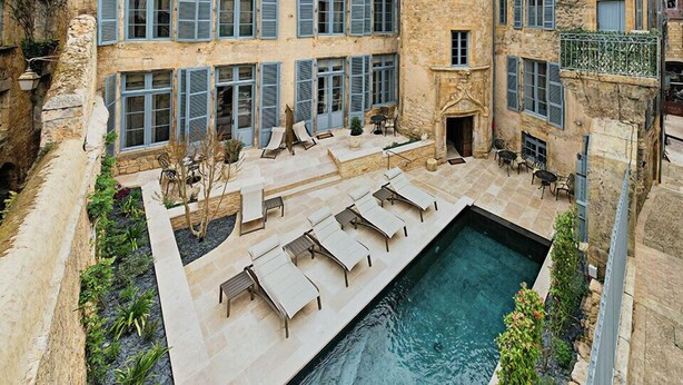 Ein Innenhof mit Swimmingpool, Liegestühlen und einem Steinhaus mit mehreren Fenstern und einem Turm.