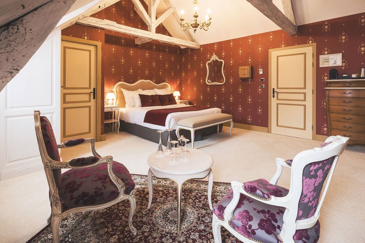 A bedroom with a bed, two chairs, a small table, and a chandelier.