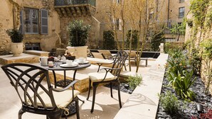 Eine Terrasse im Freien mit Tischen und Stühlen, umgeben von Steinbauten und Pflanzen.