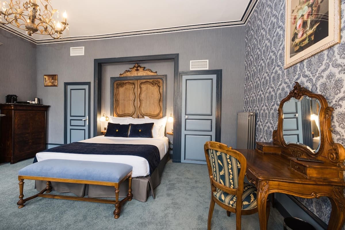 A bedroom with a large bed, a wooden dresser, a chair, and a mirror.