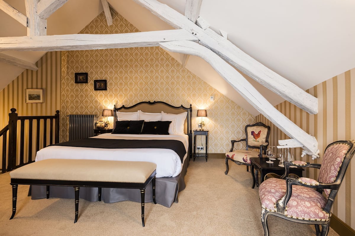A bedroom with a large bed, a bedside table with a lamp, a chair, and a small table with a decorative item.