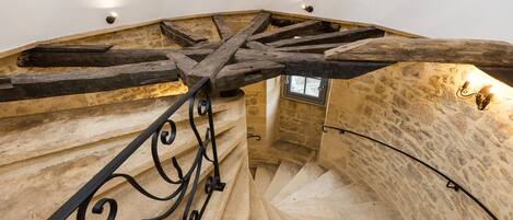 A spiral staircase with stone walls and wooden beams, featuring a wrought iron railing.