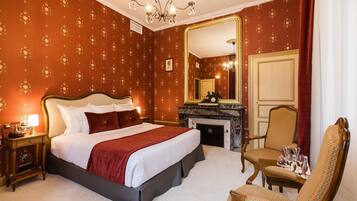 A hotel room with a large bed, a sitting area with a chair, a fireplace, and a large mirror.