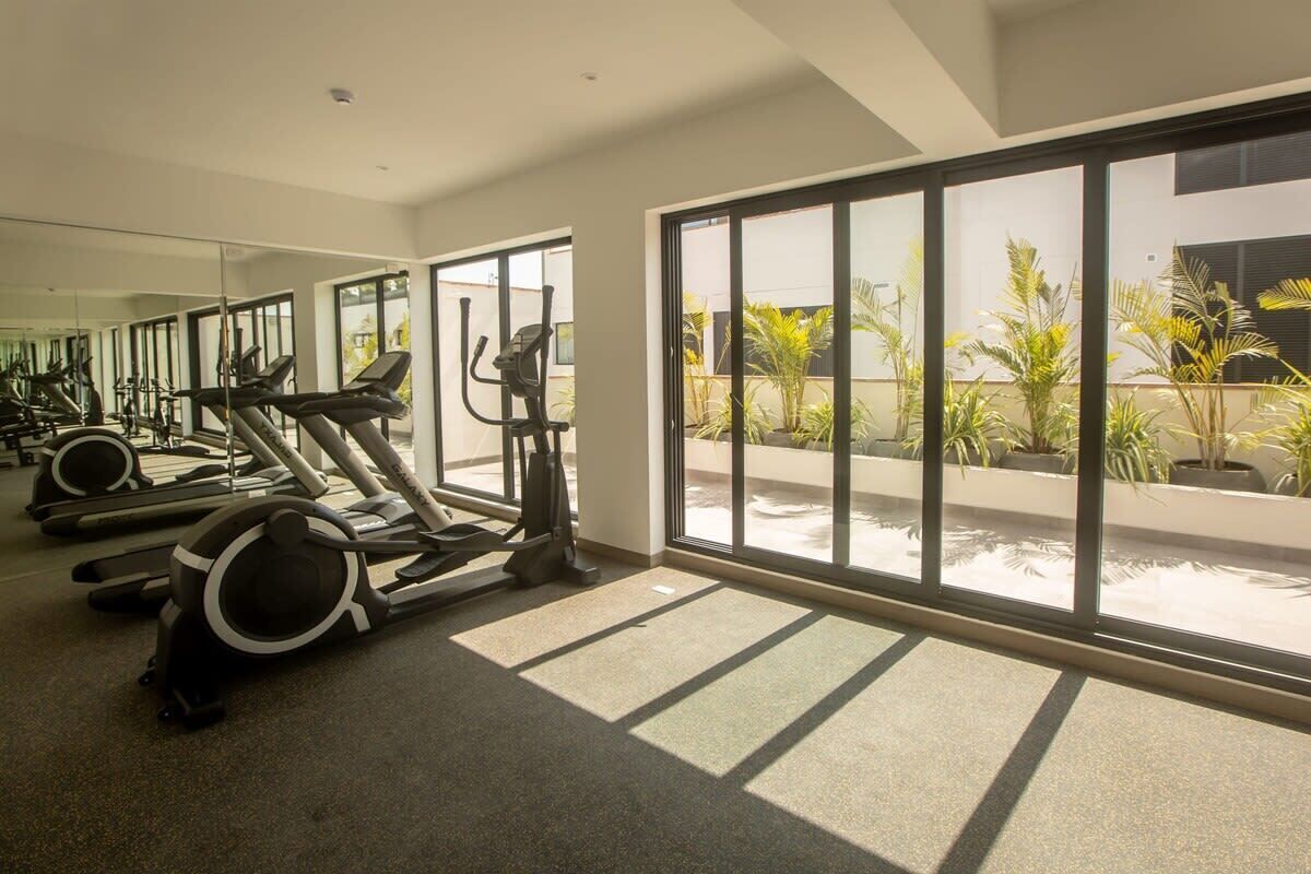 A gym with exercise equipment and large windows overlooking a courtyard with plants.