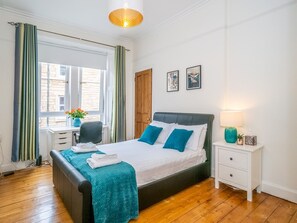 A bedroom with a bed, bedside table, and a window with curtains. - Superb 1 Bed Flat in Traditional Victorian Building - Pass the Keys (Edinburgh)