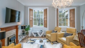 Un salón con chimenea, dos sofás de cuero, una araña y un televisor.