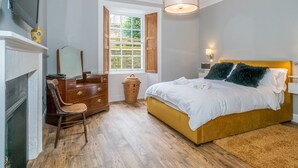 Un dormitorio con cama, cómoda, silla, ventana y chimenea.