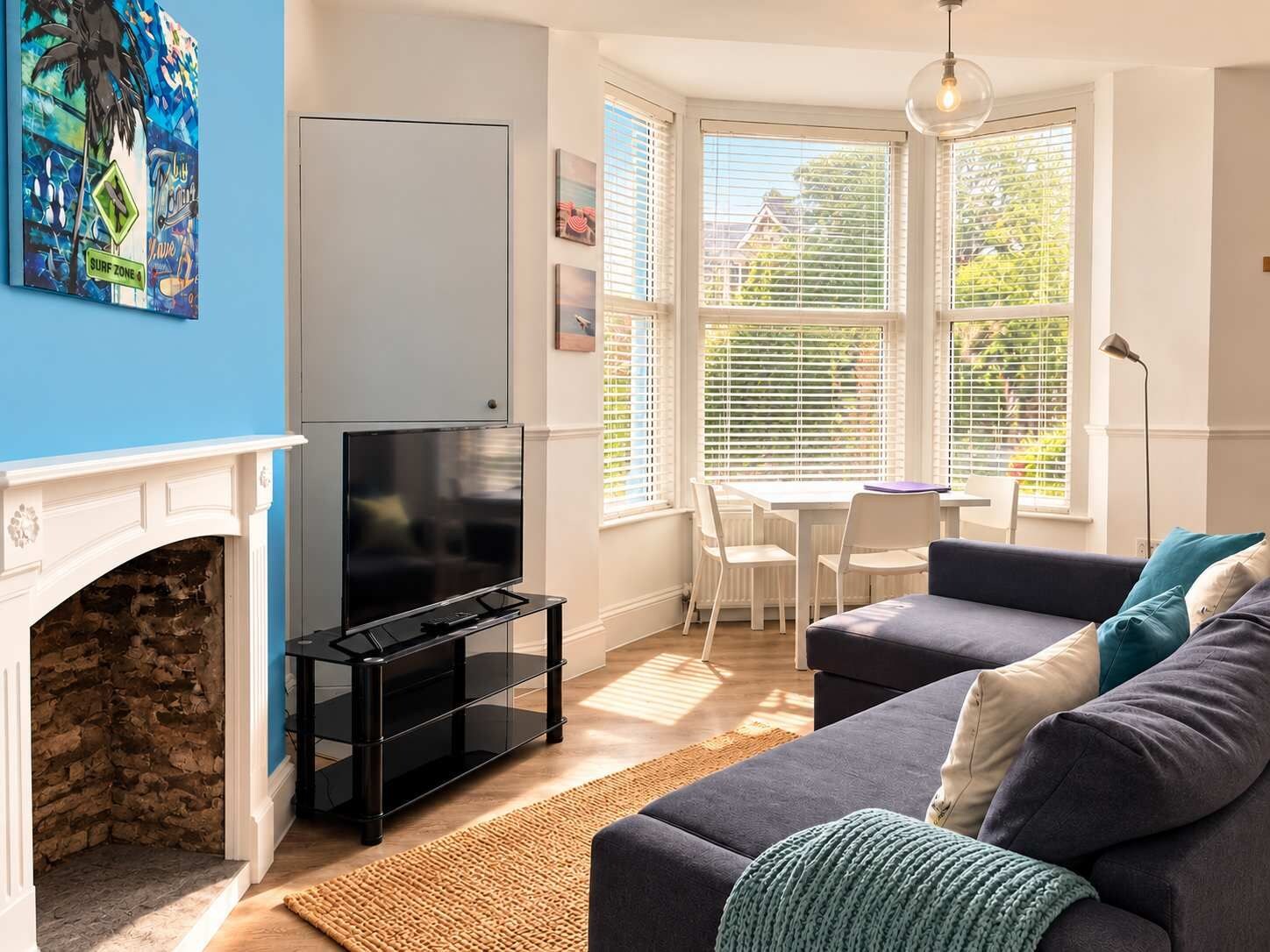 A living room with a fireplace, a television on a stand, a sofa, and a dining area with a table and chairs.