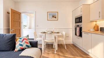 A compact living space with a dining area, kitchenette, and a sofa with a colorful pillow.