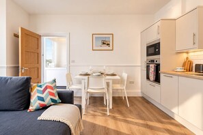 A compact living space with a dining area, kitchenette, and a sofa with a colorful pillow.