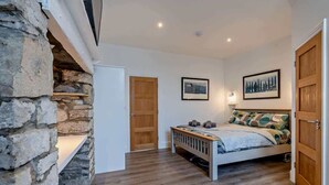 A bedroom with a stone wall, a wooden door, a bed with pillows, and two framed pictures on the wall. - Dizzy Lows Sea View Apartment Swanage Town & Beach (Swanage)
