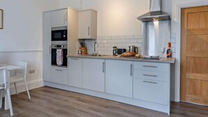 A modern kitchen with white cabinets, a stainless steel range hood, and a wooden floor. - Dizzy Lows Sea View Apartment Swanage Town & Beach (Swanage)