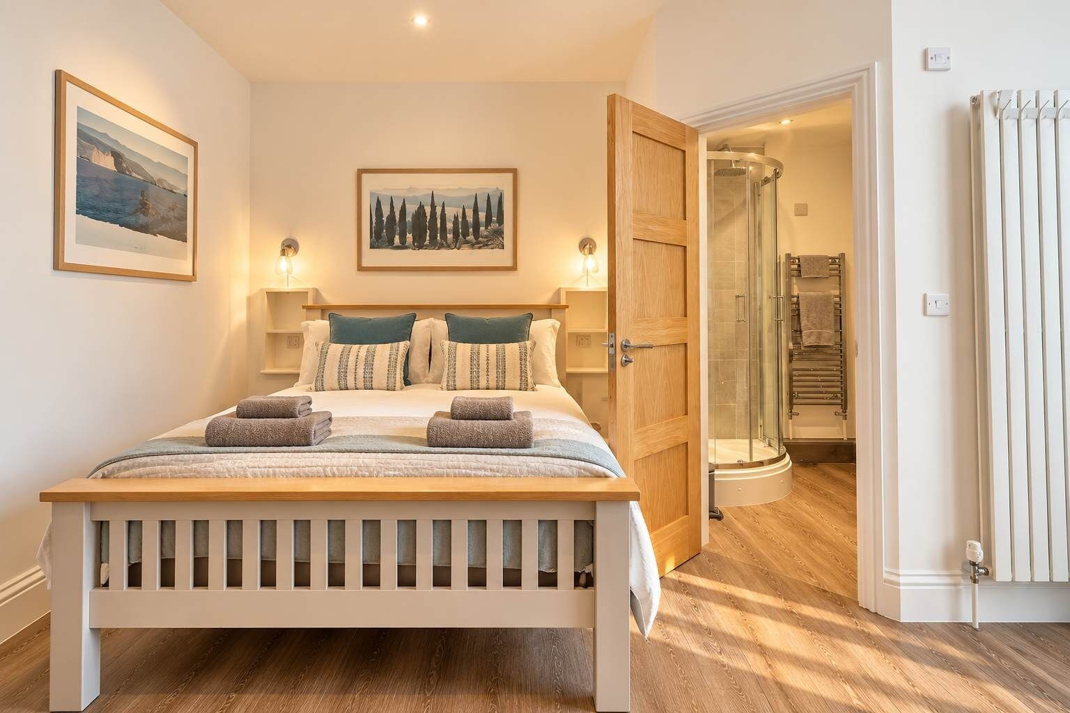 Une chambre à coucher comprenant un lit, deux tables de chevet, une commode, une grande fenêtre et une porte donnant sur une salle de bain.