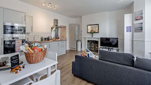 A modern kitchen with a microwave, stove, and a dining area with a basket of snacks. - Dizzy Lows Sea View Apartment Swanage Town & Beach (Swanage)