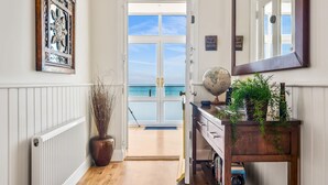 A hallway with a view of the sea, a globe, and a wooden cabinet with plants. - Jarrahdale Beach House - Stunning Luxurious Pad by the Beach - Pass the Keys (Herne Bay)