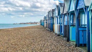 A row of beach huts with a pebble beach and the sea in the background. - Jarrahdale Beach House - Stunning Luxurious Pad by the Beach - Pass the Keys (Herne Bay)