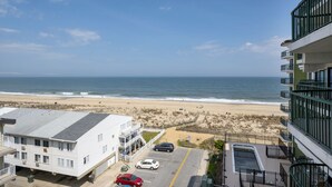 A beachfront hotel with a view of the ocean, a parking lot, and a sandy beach area. - Summer Beach 608 by Seaside Vacations & Sales (Ocean City)
